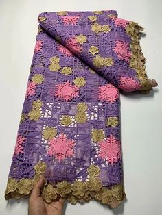 a hand is holding up a purple and gold lace with pink flowers on the edge