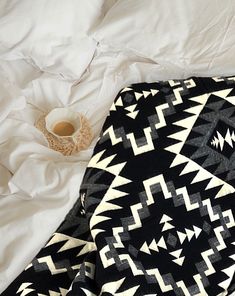 a black and white blanket sitting on top of a bed next to a cup of coffee