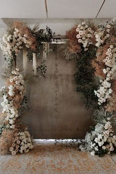 an arrangement of flowers and greenery in front of a concrete wall for a wedding ceremony