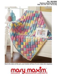 a colorful blanket sitting on top of a bed next to a white table and lamp