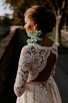 the back of a woman's wedding dress with lace and flowers on her hair