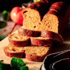 sliced loafs of bread sitting on top of a wooden cutting board next to vegetables