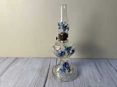 a glass vase with blue and white flowers on it sitting on a table next to a wall