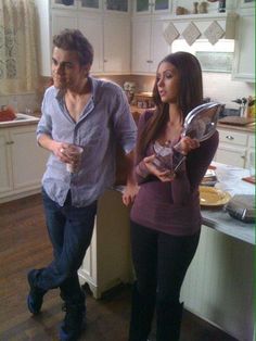 a man and woman standing in a kitchen holding plates with food on them while looking at each other