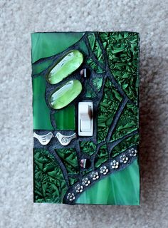 a light switch cover with green and black designs on the wall next to a white carpet