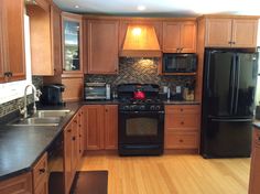 a kitchen with wooden cabinets and black appliances in it's center island, along with hardwood flooring