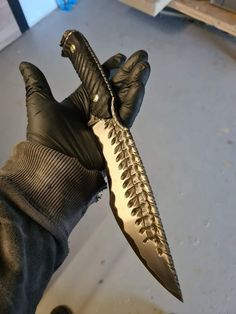 a person wearing black gloves holding a knife in their left hand with gold accents on it