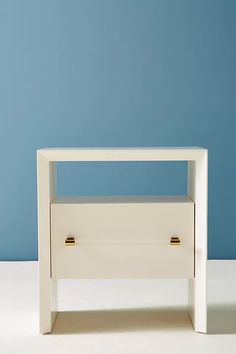 a small white table with two drawers on one side and a blue wall in the background