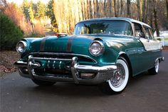 an old green and white car parked on the side of the road in front of some trees