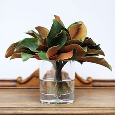 a glass vase filled with water and flowers on top of a wooden table next to a mirror