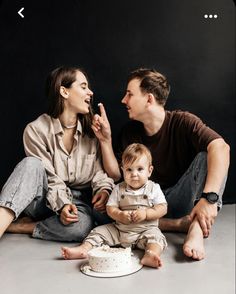 a man and woman sitting on the floor with a baby in front of them eating cake