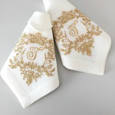 two white napkins with gold embroidered designs on them