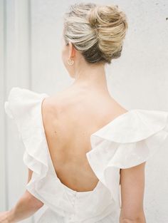 a woman wearing a white dress with ruffles on the back and gold hoop earrings