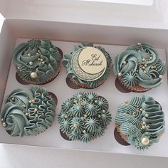 six cupcakes in a box decorated with blue icing and green frosting