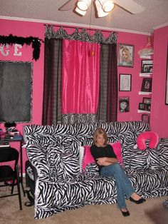 a woman sitting on top of a zebra print couch in a living room with pink walls