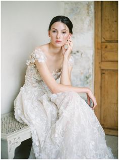 a woman in a wedding dress sitting on a bench with her hand to her face