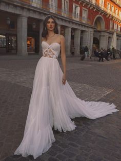 a woman in a white wedding dress standing on a brick road with buildings in the background