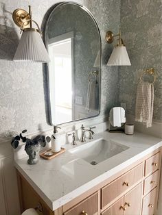 a bathroom vanity with a mirror and two lights on the wall next to it is decorated in gold