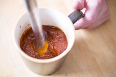 a person stirring sauce in a cup with a spoon