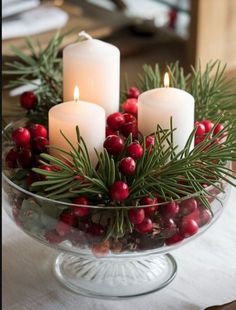 three candles are lit in a glass bowl with holly berries and pine cones on the table