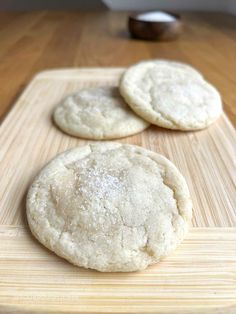 three white cookies sitting on top of a wooden cutting board