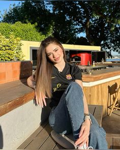 a young woman sitting on top of a wooden bench next to a table with chairs