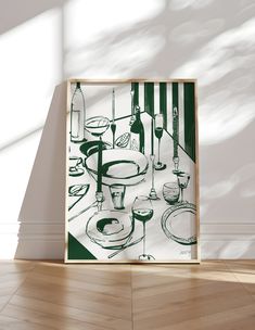 an art print is displayed on the floor in front of a wall with wine glasses and plates