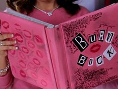 a woman is reading a pink book with the words burn book written on it and lips drawn all over it