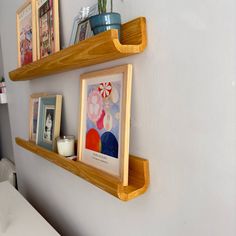 two wooden shelves with pictures on them in the corner next to a white wall and a bed