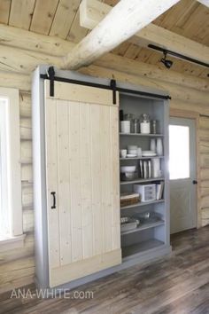 the interior of a small log cabin with open doors and shelving unit in it