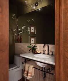 a bathroom with a sink, toilet and mirror in it's corner area next to a potted plant