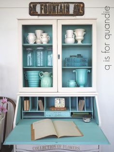 an open book is sitting on top of a blue desk with books and vases