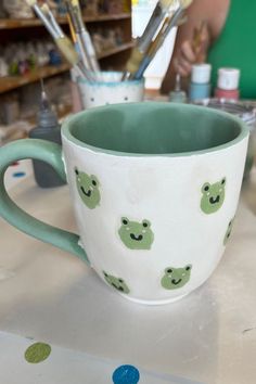 a green and white cup sitting on top of a counter next to paintbrushes