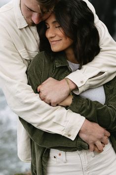 a man and woman hugging each other by the water