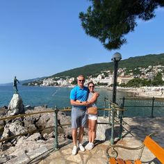 a man and woman standing next to each other near the ocean on a sunny day