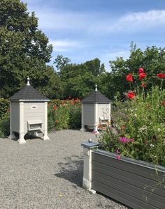 there are two small garden structures in the middle of this graveled area with red flowers