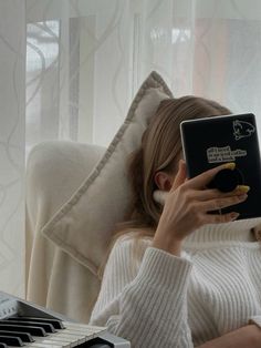 a woman sitting in front of a piano and looking at her electronic device while holding it up to her face