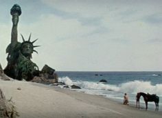 two people are standing on the beach with their horses and statue of liberty in the background