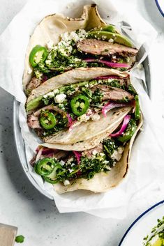 three tacos filled with meat, onions and green peppers on top of white paper