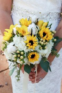 a bride holding a bouquet of sunflowers and other flowers on her wedding day