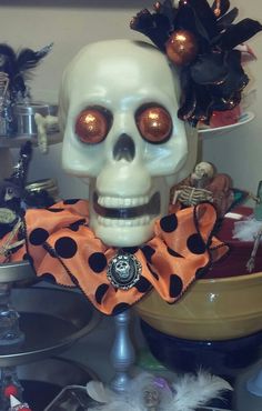 a white skull with orange eyes and black polka dots on it's collar sitting in front of a bowl full of halloween decorations