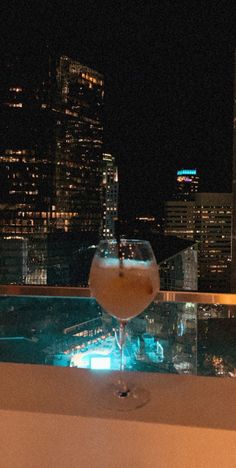 a drink sitting on top of a table in front of a cityscape at night