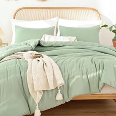 a bed with green comforter and pillows on it in front of a wooden headboard