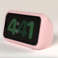 a pink alarm clock with green numbers on the front and back sides, sitting on a white surface