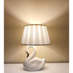 a white swan lamp sitting on top of a table next to a lampshade