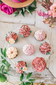 cupcakes decorated with pink and white frosting on a plate next to flowers