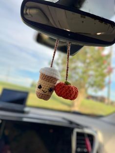 two crocheted coffee cups hanging from a car's rearview mirror