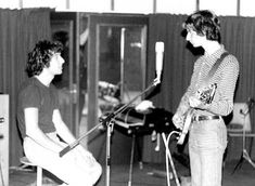 two young men sitting in front of microphones with guitars on the floor next to them