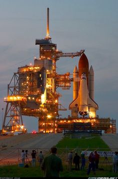 the space shuttle is lit up at night with people standing around and taking pictures in front of it