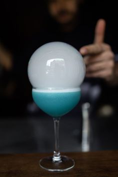 a blue and white drink sitting on top of a wooden table next to a person